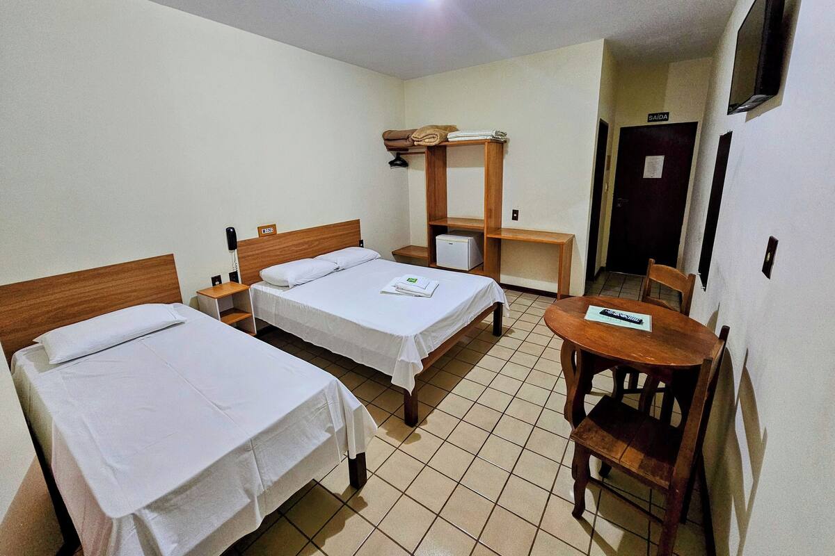 Habitación de hotel con dos camas individuales, un escritorio de madera, una silla, una mesita y un televisor en la pared.