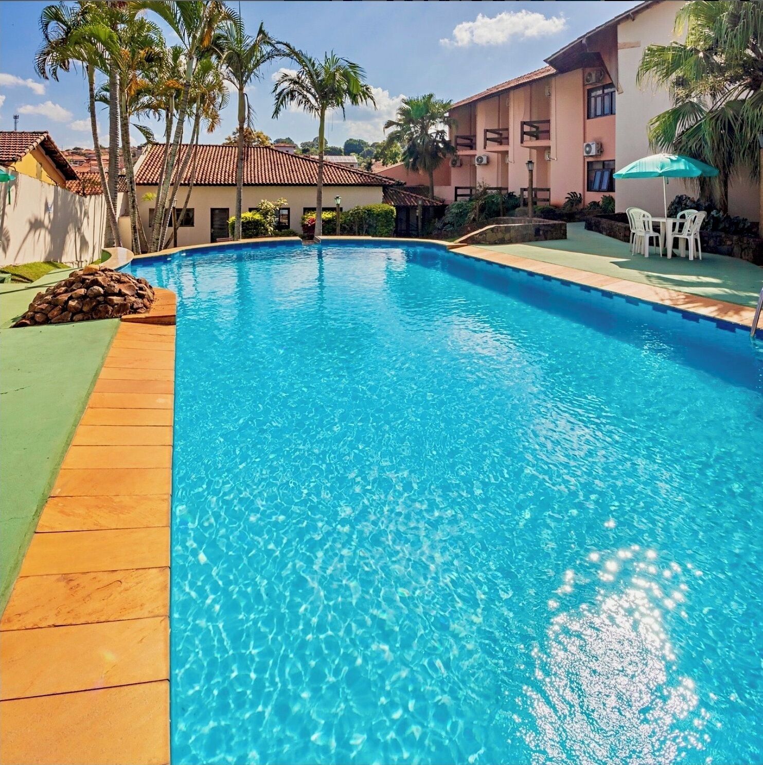 Piscina azul límpida rodeada por palmeiras e um edifício com varandas.