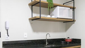 Une cuisine compacte équipée d’un lave-vaisselle encastré, d’un four à micro-ondes et d’une cuisinière. On y trouve un meuble en bois et une petite étagère avec une plante.