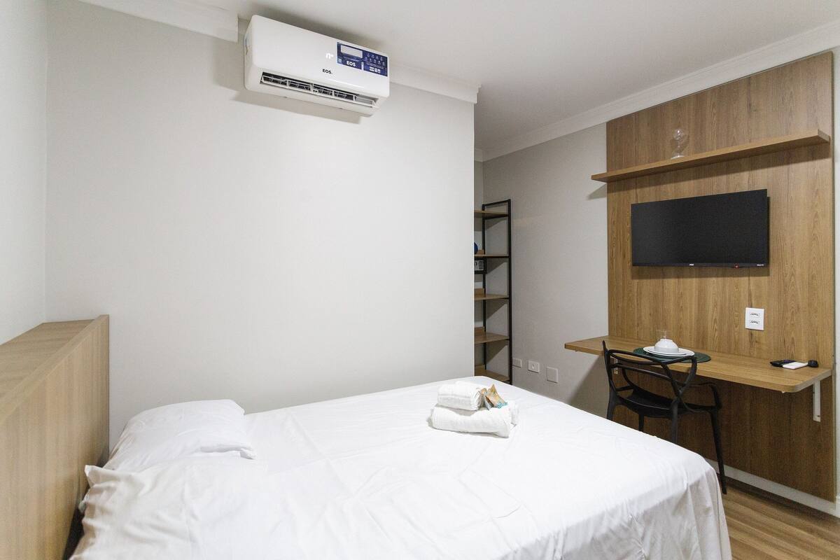 Een hotelkamer met een bed, een bureau, een stoel, een televisie en een airconditioning.