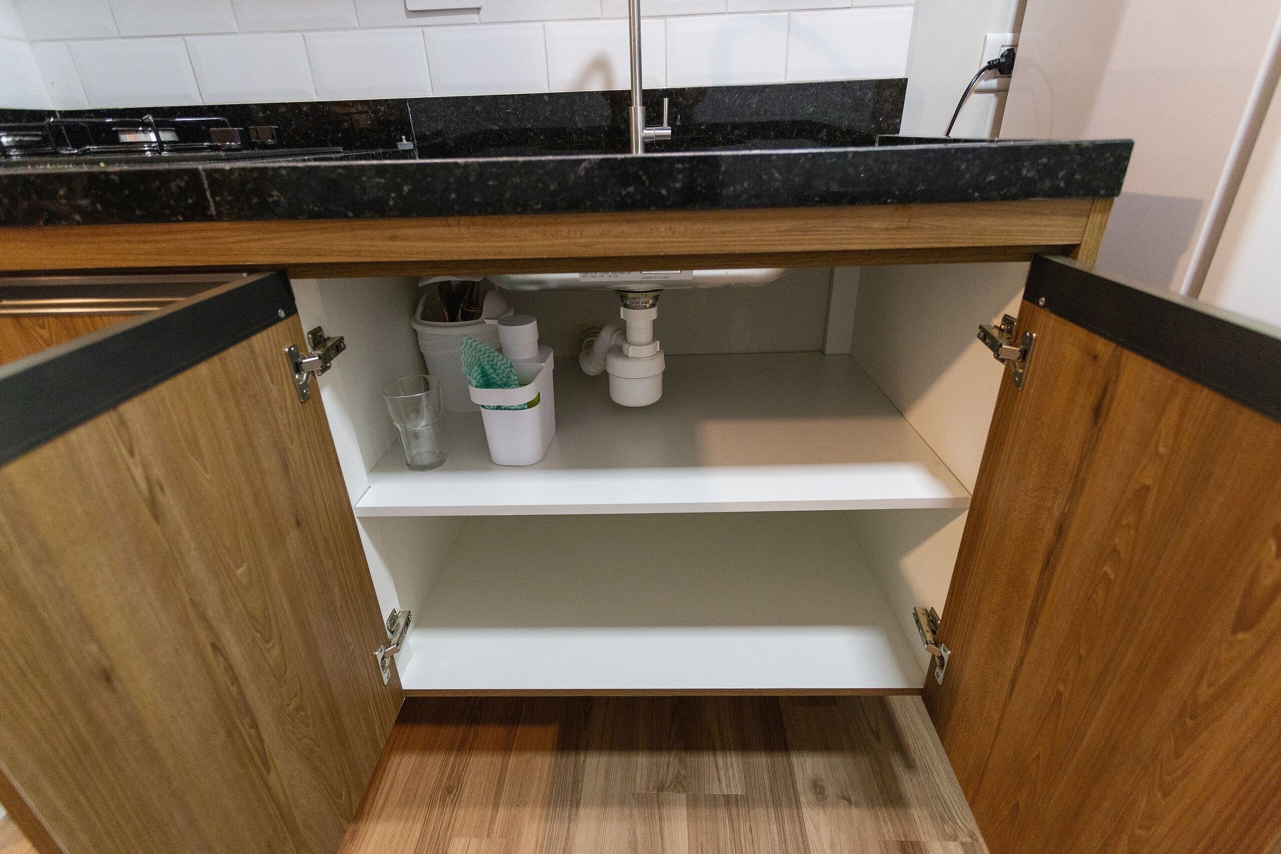 Een keuken met een zwart aanrecht, houten kastjes en een witte plank.
