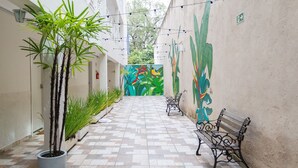 Un couloir étroit au sol carrelé, agrémenté de plantes en pot et de bancs.