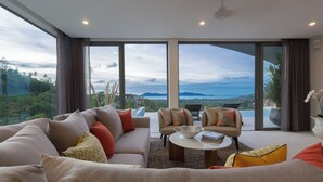 A modern living room with a large sofa, two armchairs, and a coffee table. There are large windows offering a view of the outdoors. - ZOG Villas (Koh Samui)