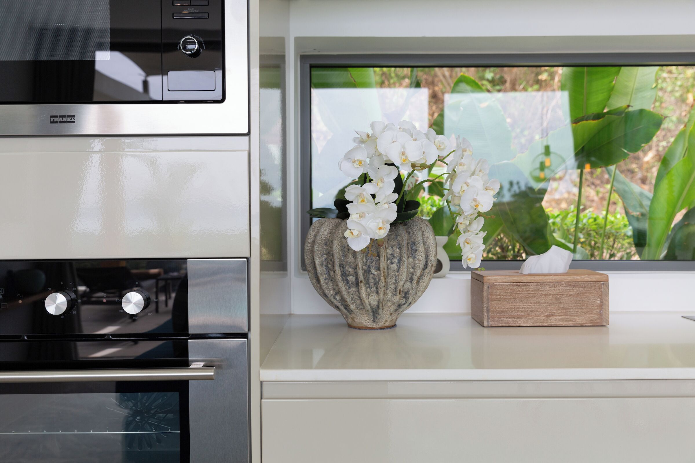 A kitchen with a microwave, oven, and a window with a view of greenery.