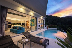 Une maison moderne dotée d’une piscine, d’un coin repas et d’un salon avec un canapé et des fauteuils.