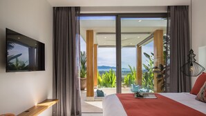 A modern bedroom with a large bed, a TV mounted on the wall, and a balcony with plants and a view of the mountains. - ZOG Villas (Koh Samui)