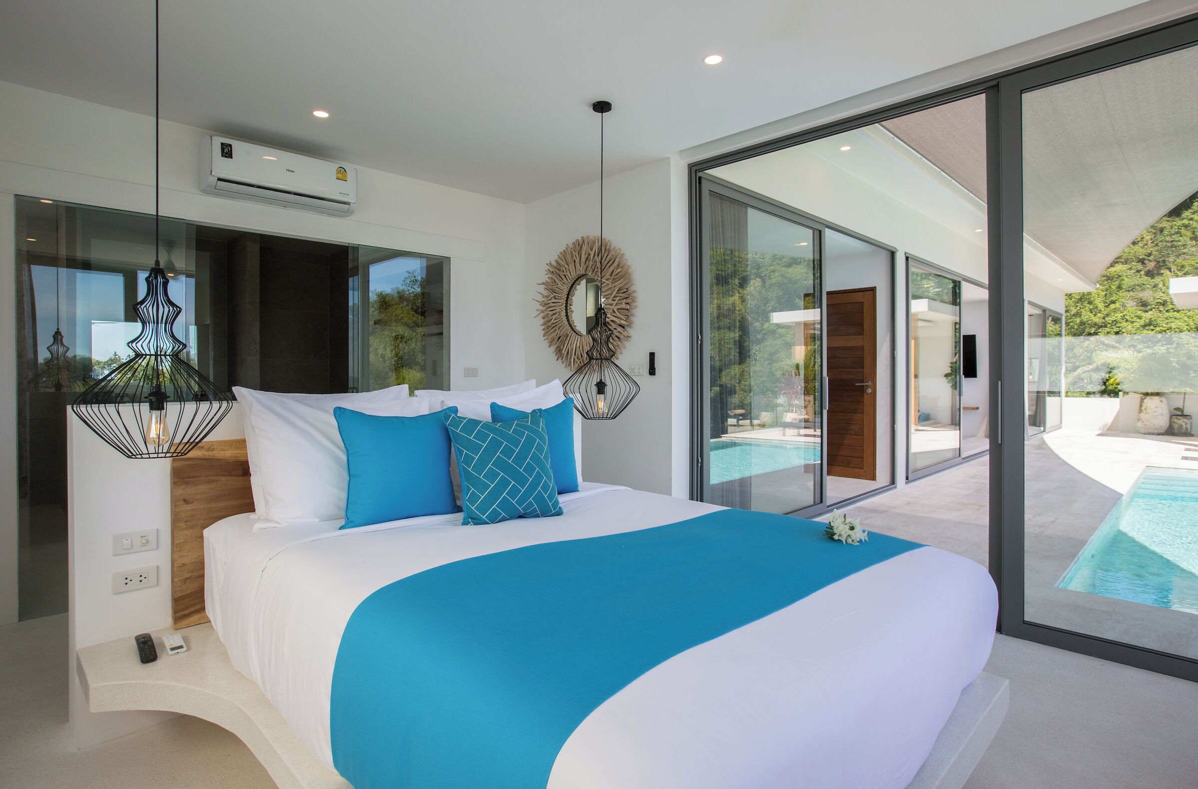 Ein modernes Schlafzimmer mit großem Bett, Blick auf einen Swimmingpool und einer Glaswand.