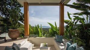 A balcony with a seating area, a large potted plant, and a view of the landscape. - ZOG Villas (Koh Samui)