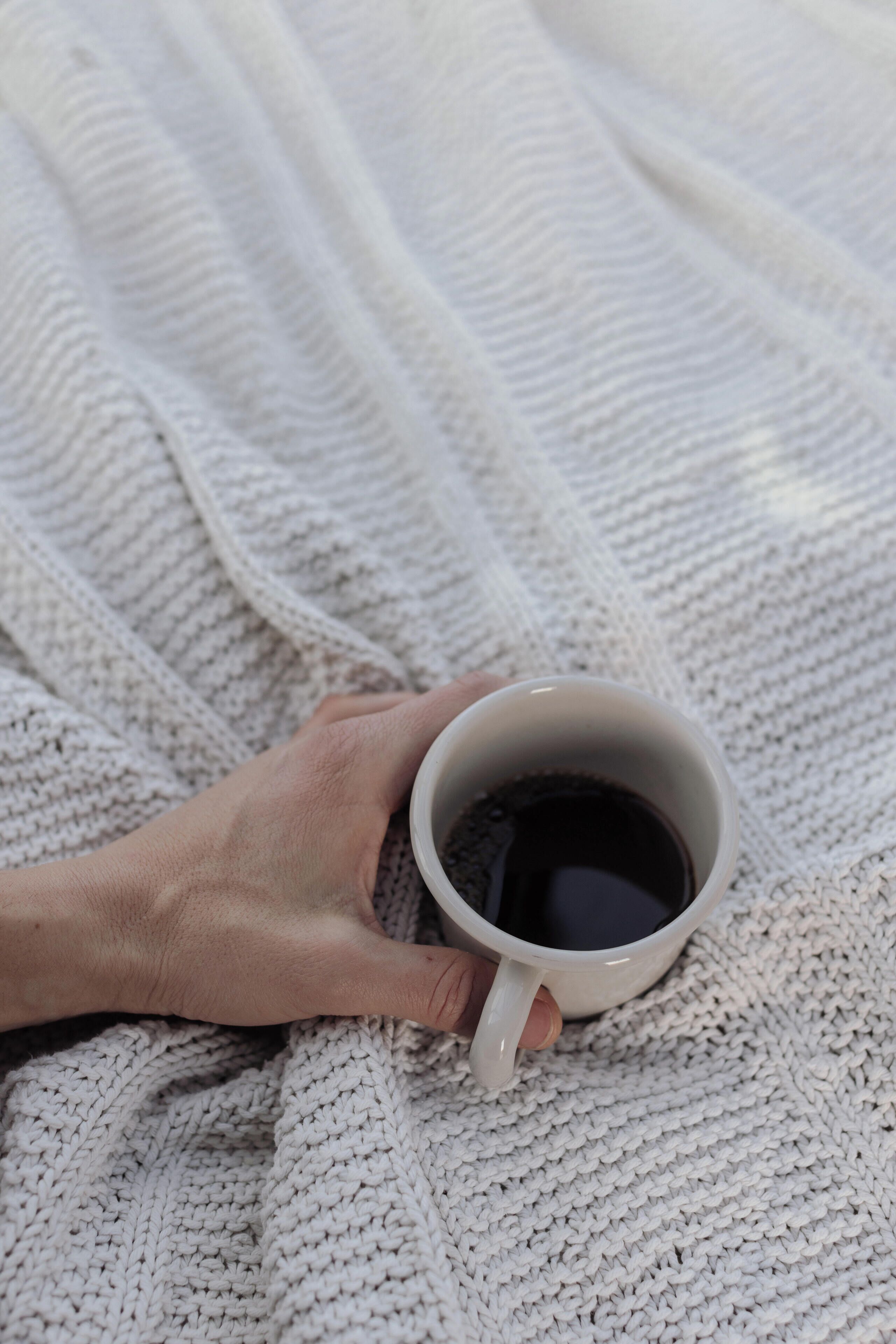 A hand holding a white mug on a knitted blanket.