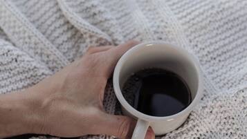 A hand holding a white mug on a knitted blanket.
