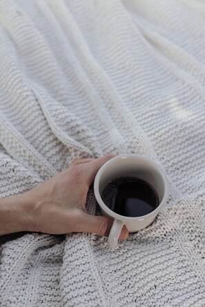 A hand holding a white mug on a knitted blanket. - Yggdrasil Igloo Water Huts Skåne (Huaröd)