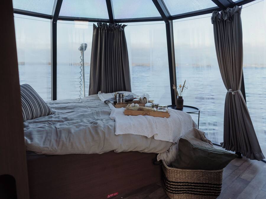 A cozy room with a bed, a small table with a tray, and a view of the water through large windows.