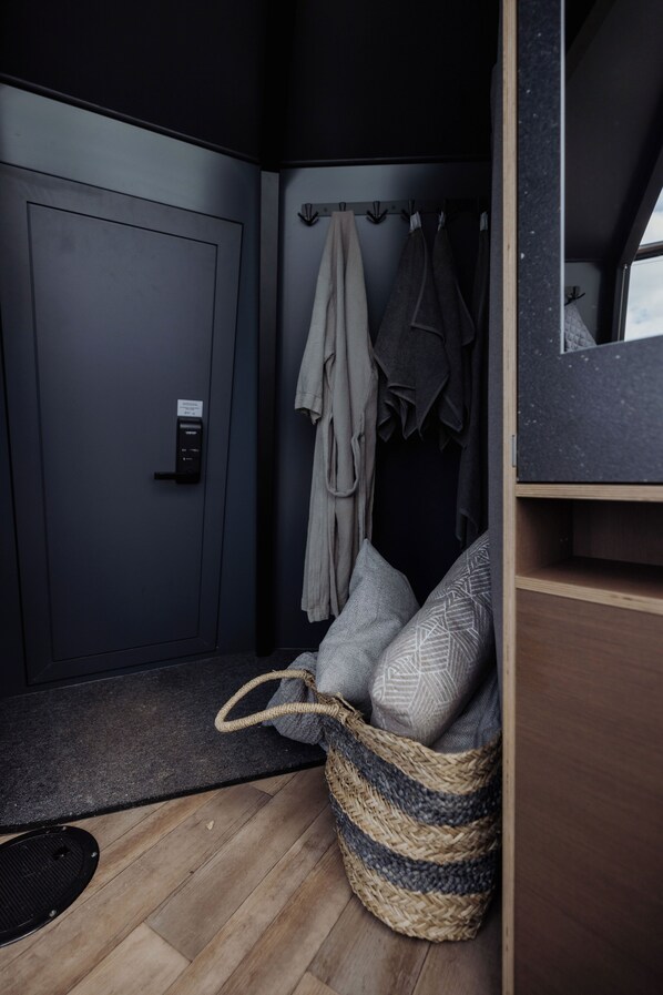 A compact bathroom with a dark door, a towel rack with towels, a woven basket, and a wooden floor. - Yggdrasil Igloo Water Huts Skåne (Huaröd)