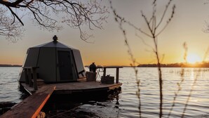 Geodeettinen kupolirakenne laiturilla, tyynen järven rannalla auringonlaskun aikaan.