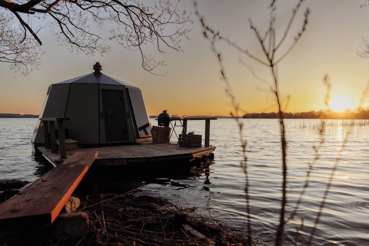 Een geodetische koepelstructuur op een steiger aan een rustig meer bij zonsondergang.