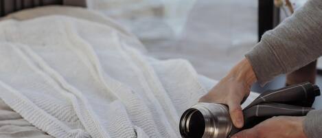 A person pouring a drink into a cup on a bed with a knitted blanket.