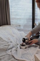 Una persona sirve una bebida en una taza sobre una cama con una manta tejida.