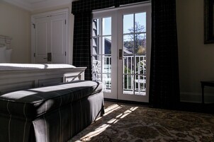 Un dormitorio con una cama grande, un banco oscuro, una alfombra estampada y vistas al exterior a través de una puerta de cristal.