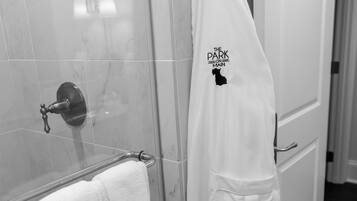 A bathroom with a glass shower enclosure, a white towel rack with two towels, and a white robe hanging on a hook.