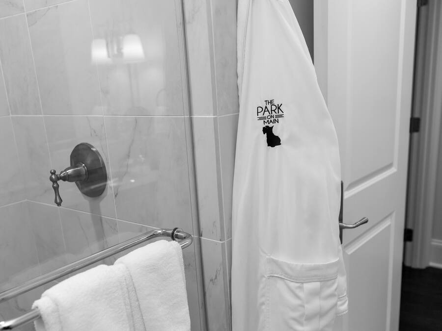 A bathroom with a glass shower enclosure, a white towel rack with two towels, and a white robe hanging on a hook.