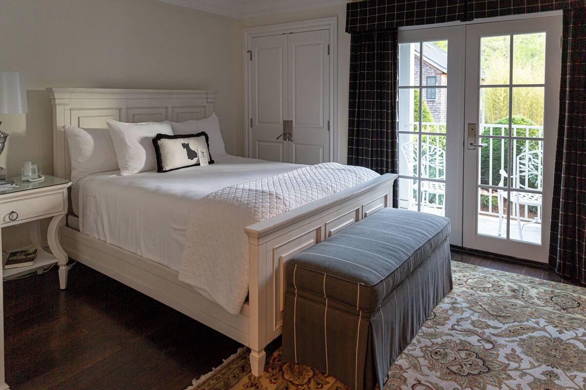 A bedroom with a bed, nightstand, bench, and a view through a door.