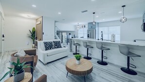 Una cocina moderna con una isla central, taburetes de bar y un comedor con sofá y sillas.