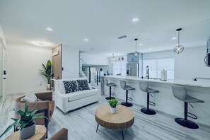 A modern kitchen with a central island, bar stools, and a dining area with a sofa and chairs. - Charming fully renovated 4-bedroom spacious house with pool in Tampa/Lutz area!  (Lutz)
