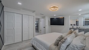 Un dormitorio moderno con una cama grande, un televisor montado en la pared y un vestidor.