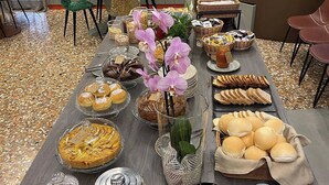 A buffet table with various food items, including pastries, bread, fruits, and a vase with flowers. - CONTRA' CONTARINI (Valbrenta)