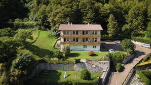A two-story building with a stone foundation, surrounded by lush greenery and a stone wall. - CONTRA' CONTARINI (Valbrenta)