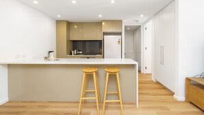 A modern kitchen with a central island, wooden stools, and a refrigerator. - Elegant & Cosy Haven in Lively Kingston Foreshore (Kingston)