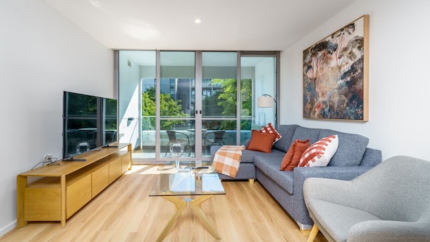 A modern living room with a sofa, a coffee table, a TV, and a large window overlooking a balcony. - Elegant & Cosy Haven in Lively Kingston Foreshore (Kingston)
