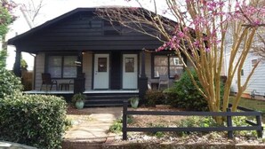 A two-story house with a porch, a front door, and a small front yard with a bench and a potted plant.