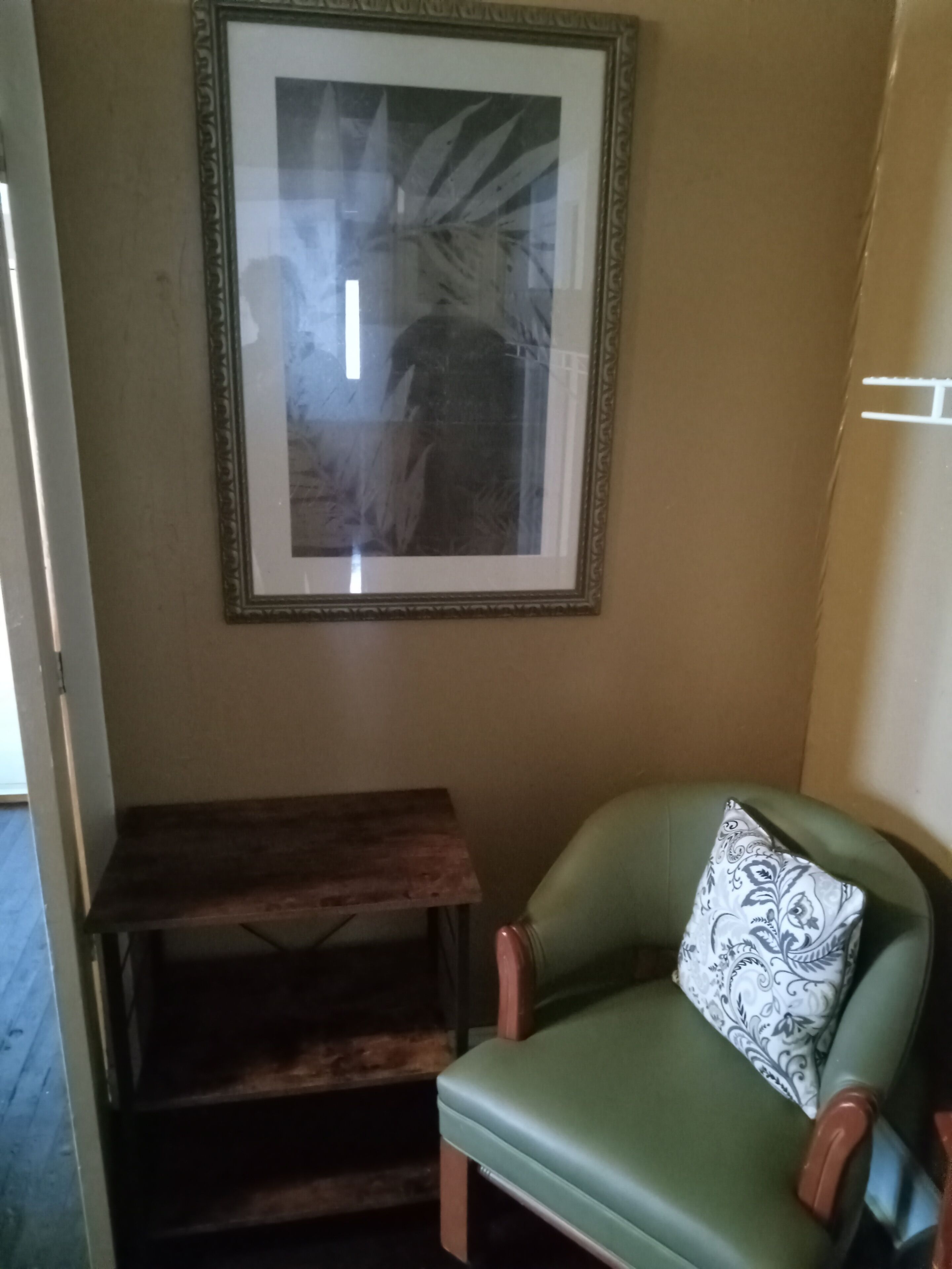 A room with a framed picture on the wall, a wooden bench, and a green chair with a patterned pillow.