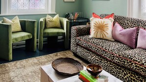 A living room with a green sofa, two armchairs, a coffee table, and a large window with decorative ironwork. - Petit Pineapple House Villa & Guesthouse (Cape Town)