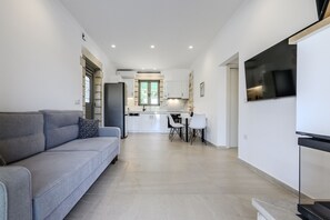 A modern apartment with a grey sofa, a dining area, and a kitchen in the background.