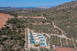 An aerial view of a resort with multiple buildings, a swimming pool area, and a hilly landscape with sparse vegetation.