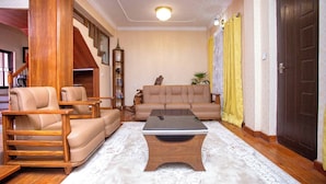 A living room with a sofa, armchairs, a coffee table, and a staircase.
