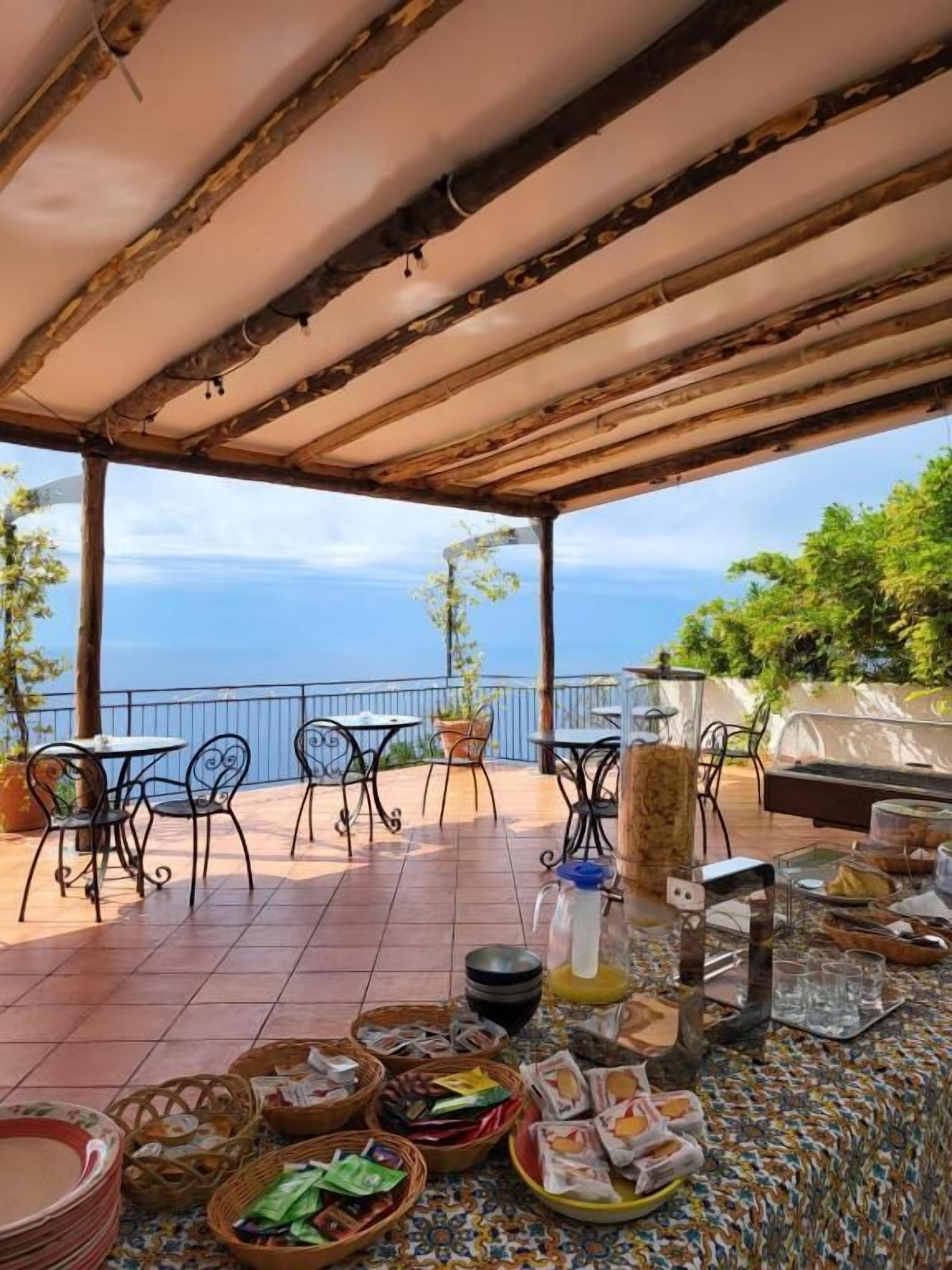 An outdoor patio with tables and chairs, a tiled floor, and a view of the sea.