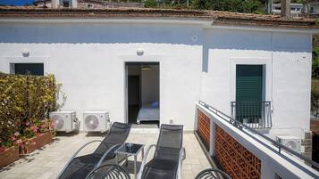 A white building with a balcony, outdoor seating, and two air conditioning units.