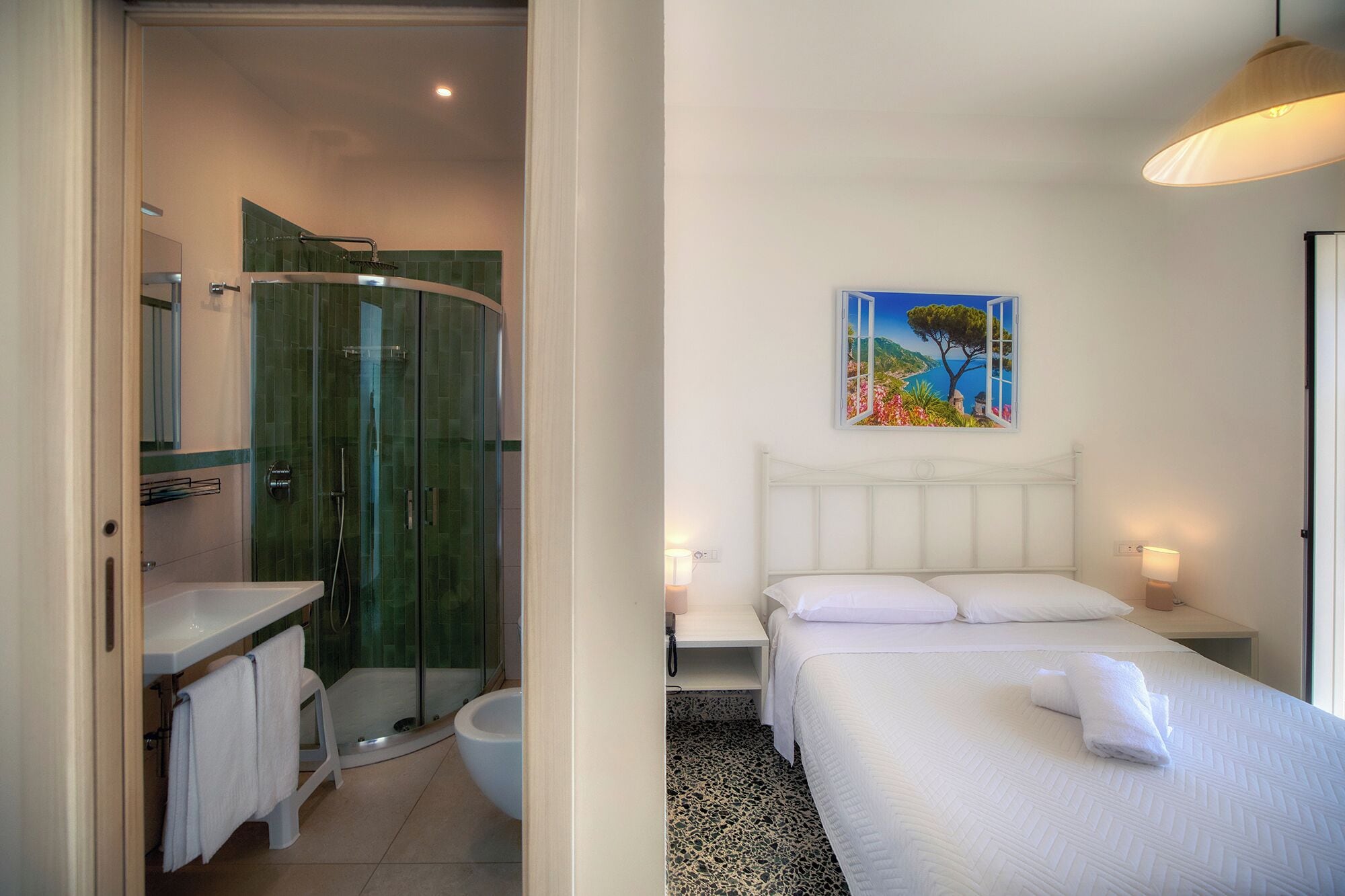 A hotel room with a shower, a bed, a painting, and a view of the sea.
