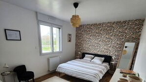 Ein Schlafzimmer mit Bett, Schreibtisch, Stuhl, Fenster und einer Wand mit Muster.
