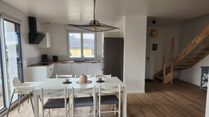 Eine moderne Küche mit weißen Schränken, einem Esstisch mit Stühlen, einem großen Fenster und einer Holztreppe.