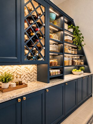 A kitchen with dark cabinetry, a wine rack, and a countertop with a plant and a bowl of fruit. - Extended-Stay Home  30, 60, 90+ Days  W/ Secure Work Trailer Parking Available (Jacksonville)
