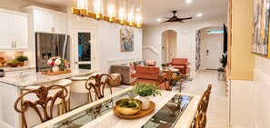 A modern kitchen with white cabinetry, a stainless steel refrigerator, and a dining area with a glass table and wooden chairs.