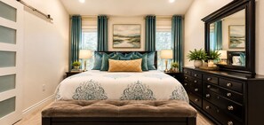A bedroom with a large bed, a dresser, a mirror, and two windows with curtains.