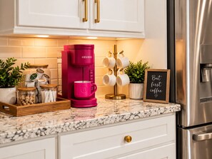A kitchen with a pink Keurig coffee maker, a coffee mug, a mug rack, a chalkboard sign, and a stainless steel refrigerator. - Extended-Stay Home  30, 60, 90+ Days  W/ Secure Work Trailer Parking Available (Jacksonville)