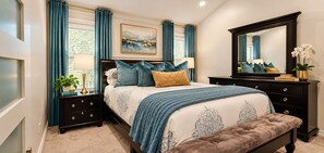 A bedroom with a bed, a nightstand, a dresser, a mirror, and a window with curtains.