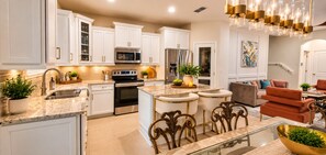 A modern kitchen with white cabinetry, stainless steel appliances, and a central island with bar stools. - Extended-Stay Home  30, 60, 90+ Days  W/ Secure Work Trailer Parking Available (Jacksonville)