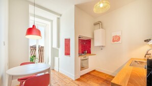 Cocina compacta con comedor, que incluye una lámpara colgante roja, un armario blanco y un backsplash con azulejos rojos.